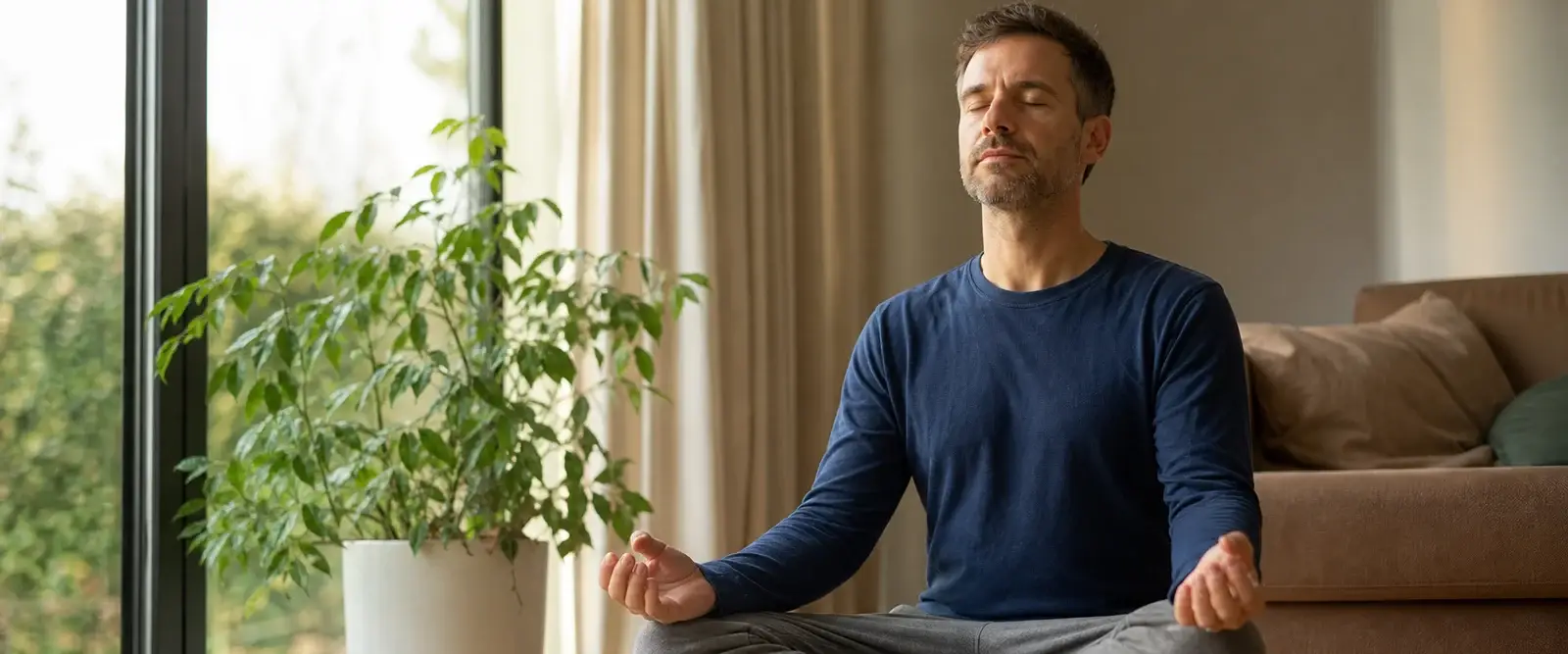 A man meditating on a cushion by a sunny window, phone face down out of reach